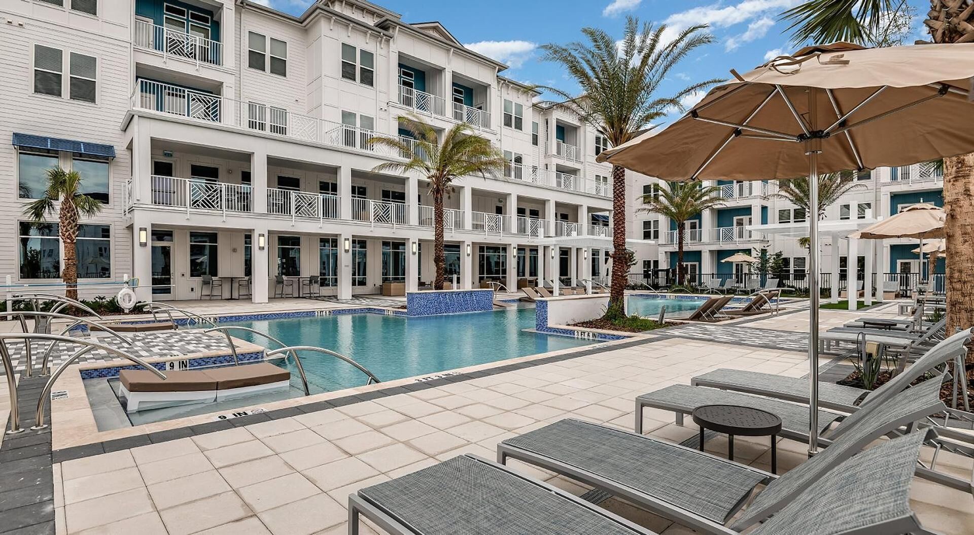 A hotel with a pool area, outdoor seating, and palm trees.