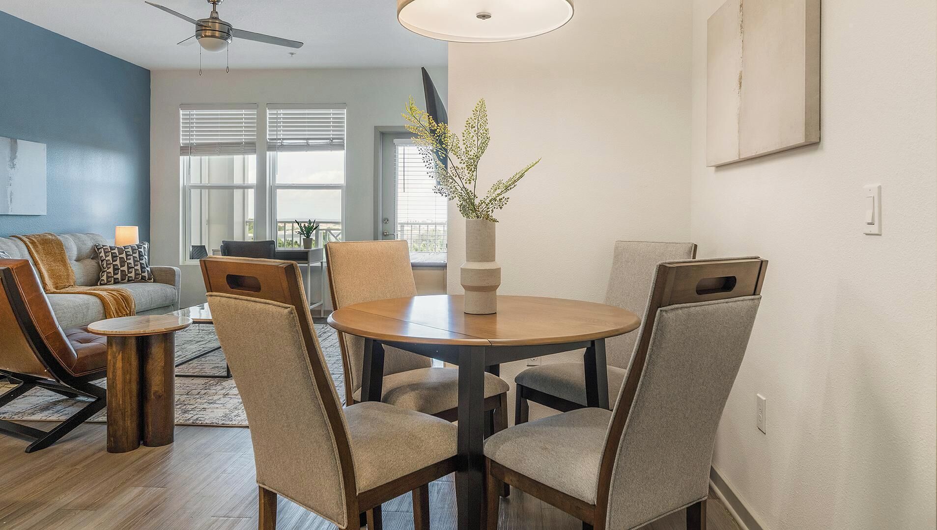 A dining area with a round table, six chairs, a vase with flowers, and a ceiling fan.