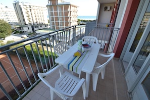 Ein Balkon mit einem weißen Tisch und Stühlen, einer gestreiften Tischdecke und einer kleinen Pflanze.