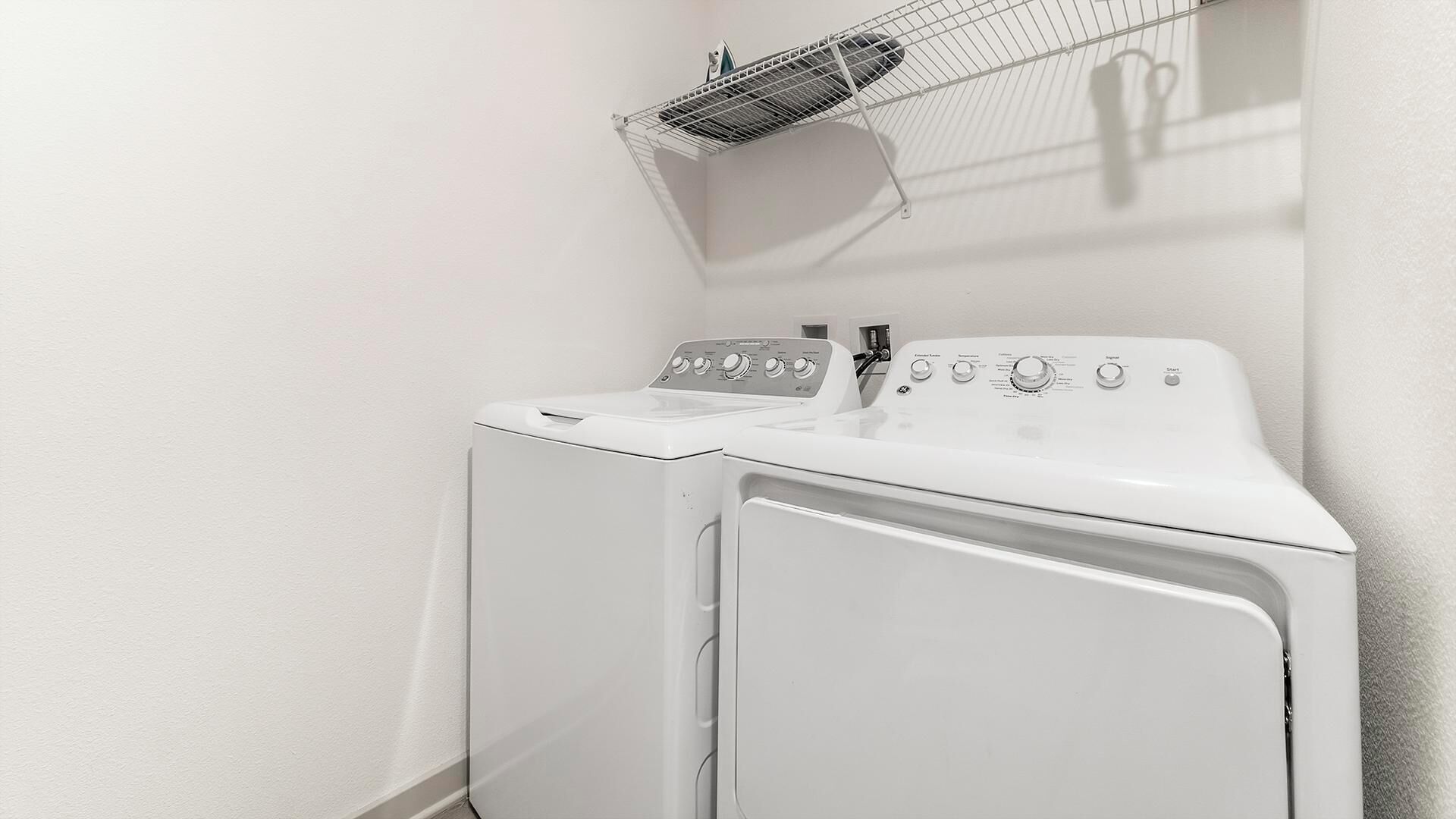 A laundry area with a washing machine and dryer, a drying rack, and a wall-mounted fan.
