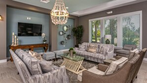 A living room with a sofa, armchairs, a coffee table, a TV, decorative wall art, and a chandelier. - Landing | Chic 2BD, Game Room, Clubhouse (Apopka)