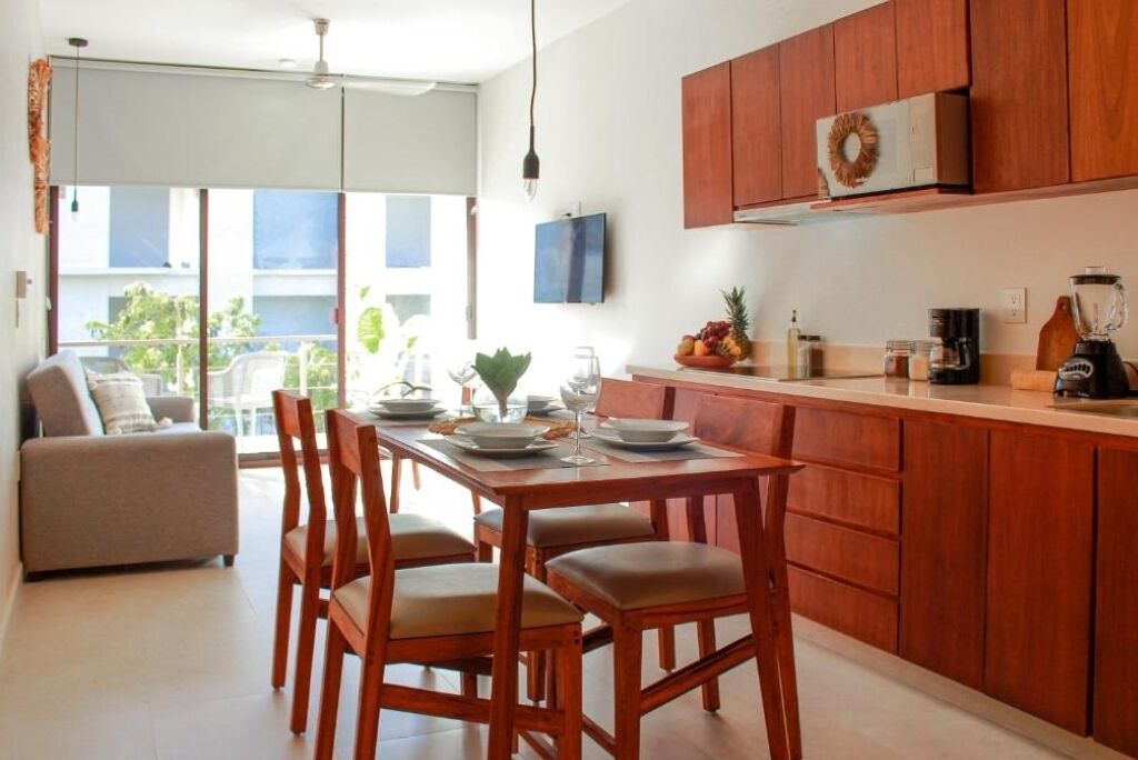 Una cocina moderna con armarios de madera, una mesa de comedor con sillas y vistas al exterior a través de amplios ventanales.