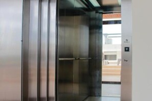 An elevator with a metallic finish and a control panel with a directional arrow. - Gama 09 Apartments - Apartment with balcony (Tulum)