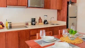 A compact kitchen with wooden cabinets, a microwave, a coffee maker, a blender, and a refrigerator. - Gama 09 Apartments - Apartment with balcony (Tulum)