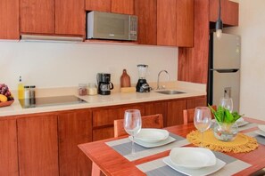A compact kitchen with wooden cabinets, a microwave, a coffee maker, a blender, and a refrigerator. - Gama 09 Apartments - Apartment with balcony (Tulum)