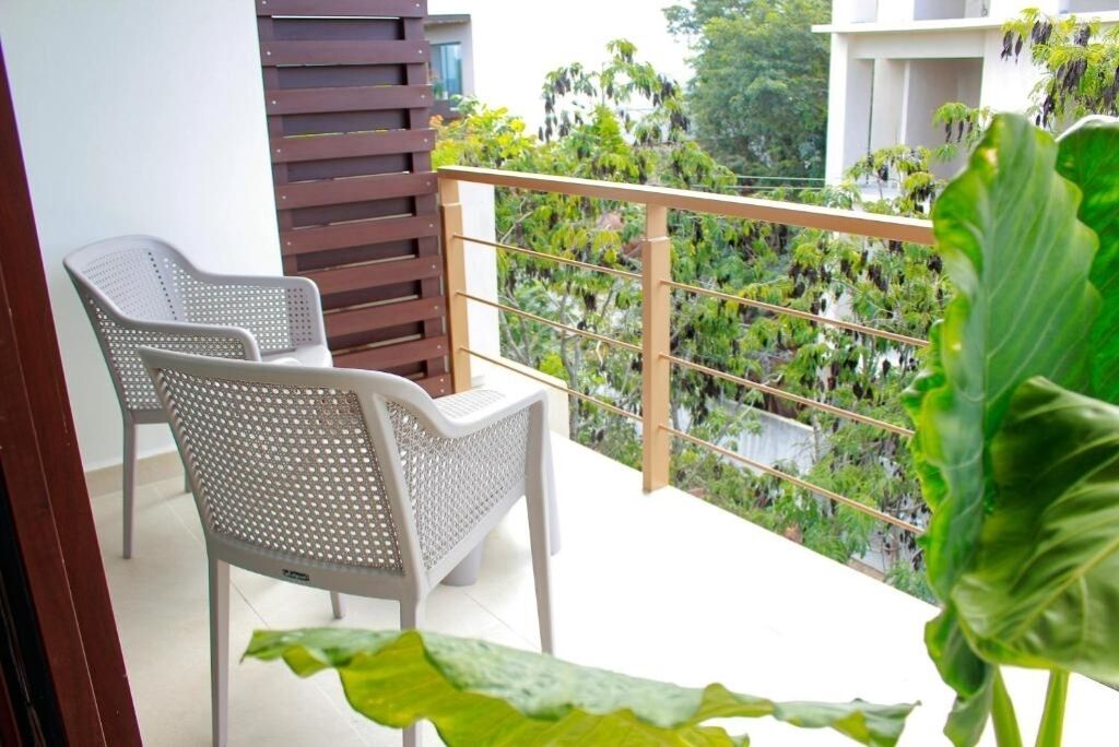 Un balcon avec deux chaises en plastique blanc, un paravent en lattes de bois et une vue sur un jardin luxuriant et verdoyant.
