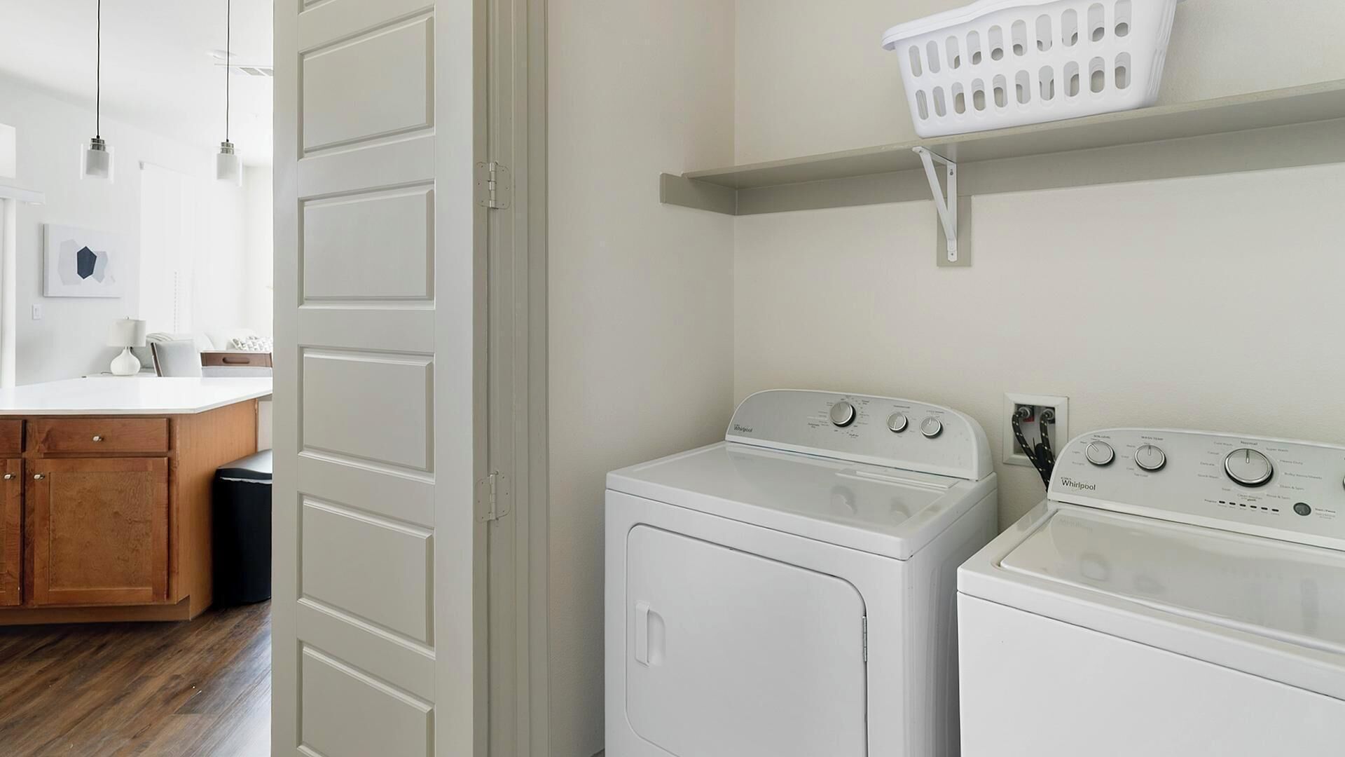 A laundry room with two white front-loading washers and dryers, a wooden cabinet, and a white laundry basket on a shelf.