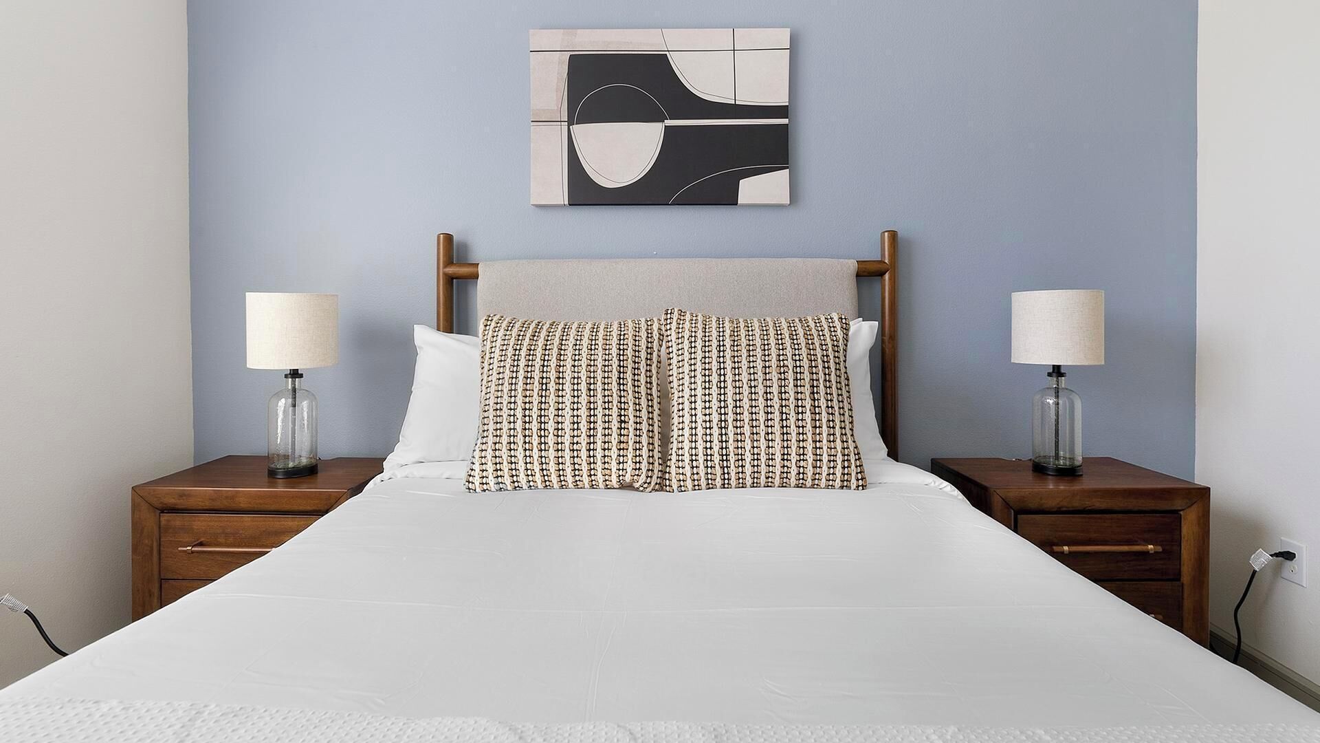 A neatly made bed with a patterned pillow, a wooden headboard, and two bedside lamps on wooden nightstands.
