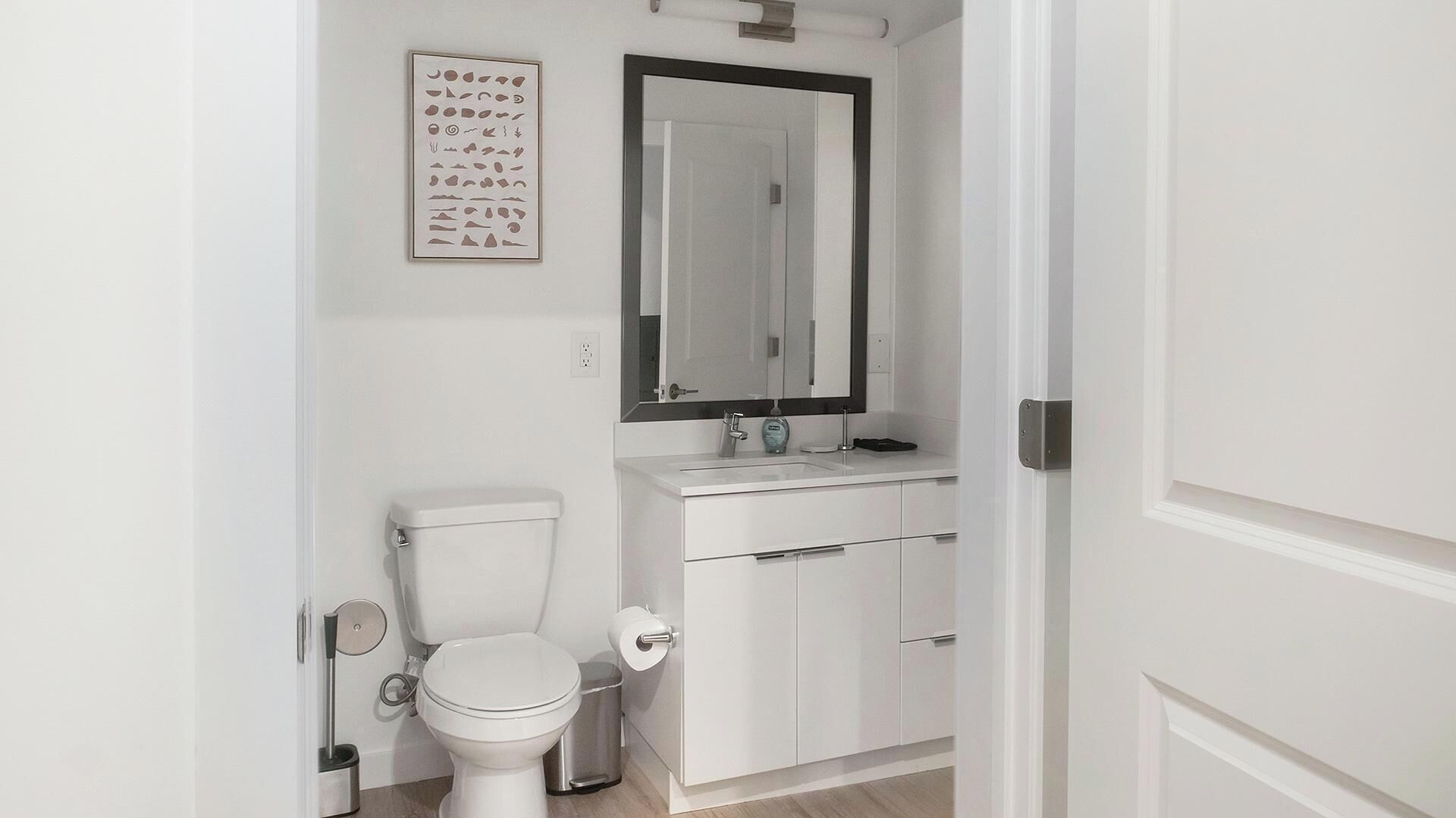 A bathroom with a toilet, sink, mirror, and cabinet.