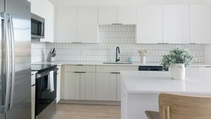 A modern kitchen with white cabinets, a stainless steel refrigerator, a microwave, a sink with a faucet, and a dishwasher. - Landing | Stunning 2BD, Gym, Game Room (Chapel Hill)