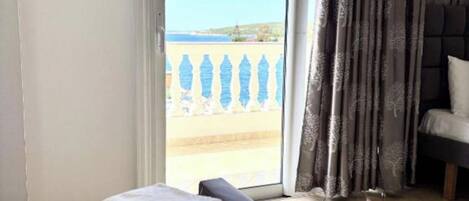 Habitación de hotel con una cama, vista al mar a través de una puerta corredera y un balcón con barandilla.