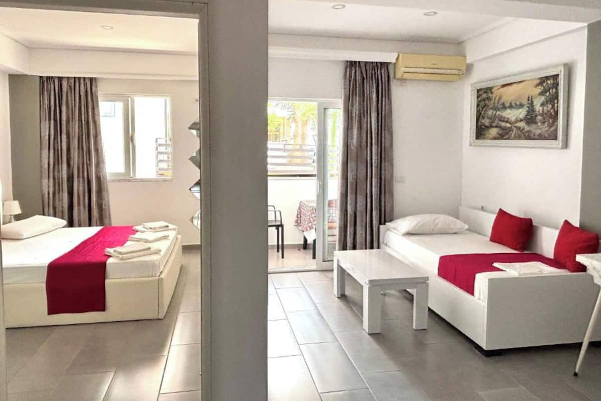 A modern hotel room with a bed, a sofa, a small table, and a painting on the wall.
