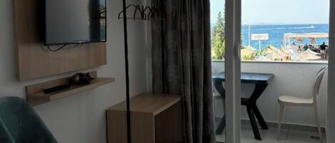 A modern room with a TV, a chair, a small table, and a balcony with a view of the sea.