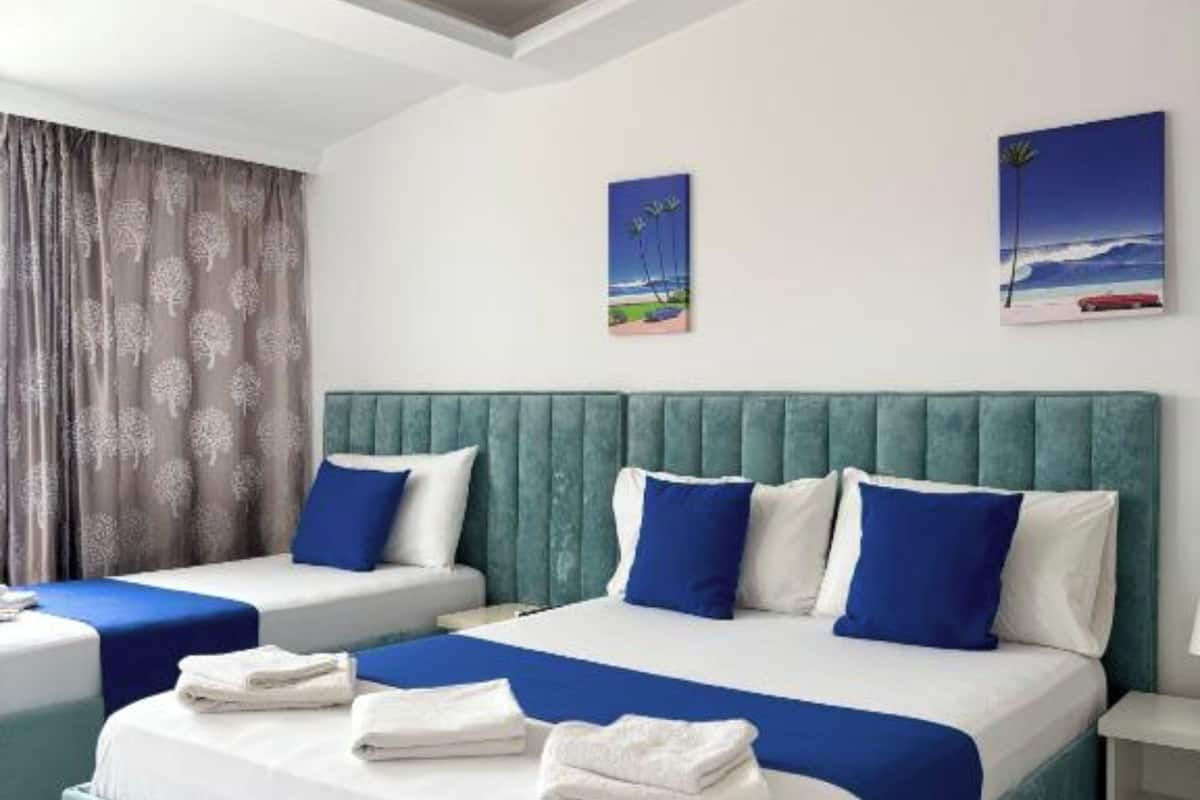 A hotel room with two beds, each with blue and white bedding, a teal upholstered headboard, and artwork on the walls.