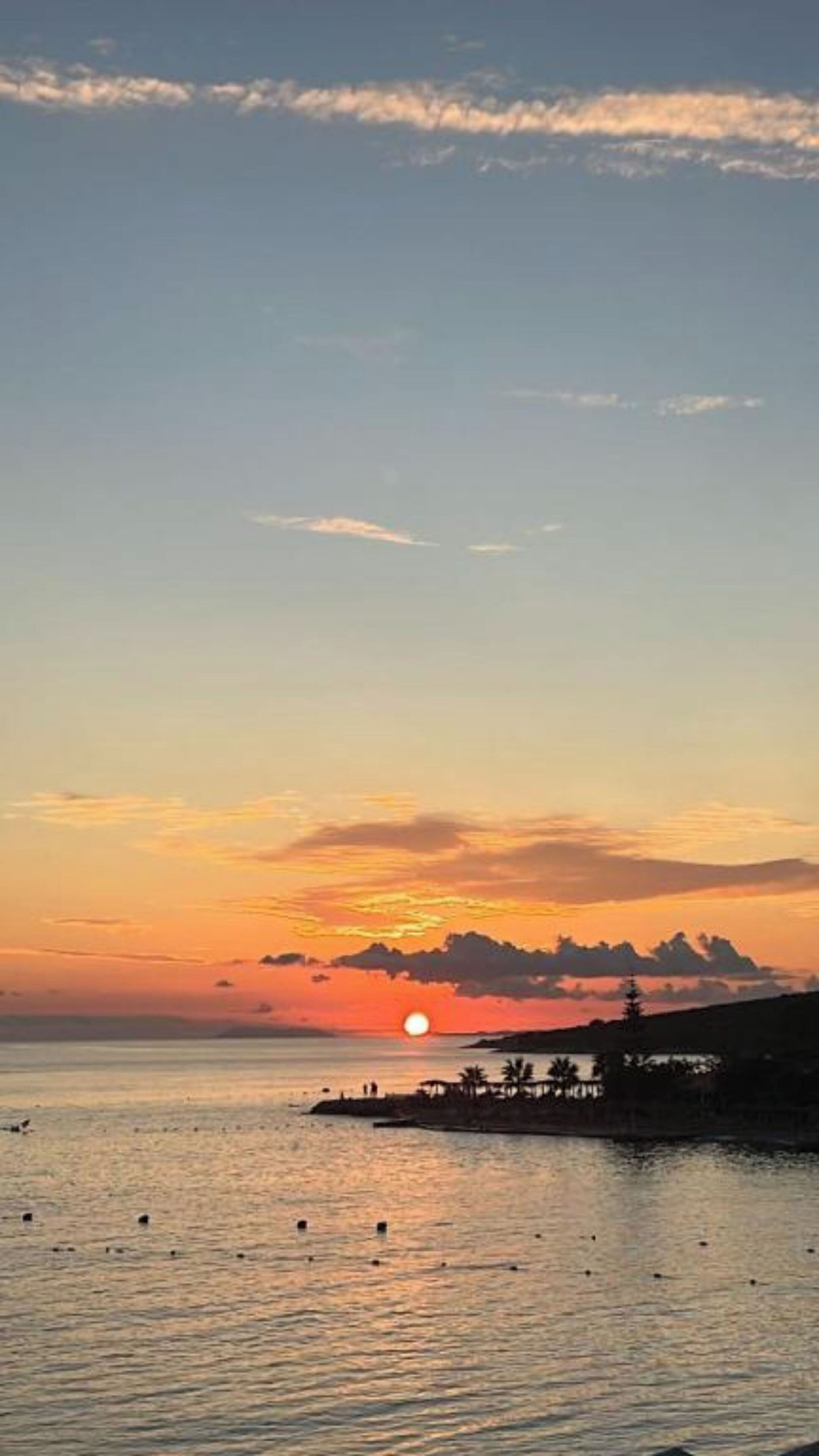 Un atardecer sobre aguas tranquilas, con la silueta de una zona costera y una pequeña construcción en la orilla.