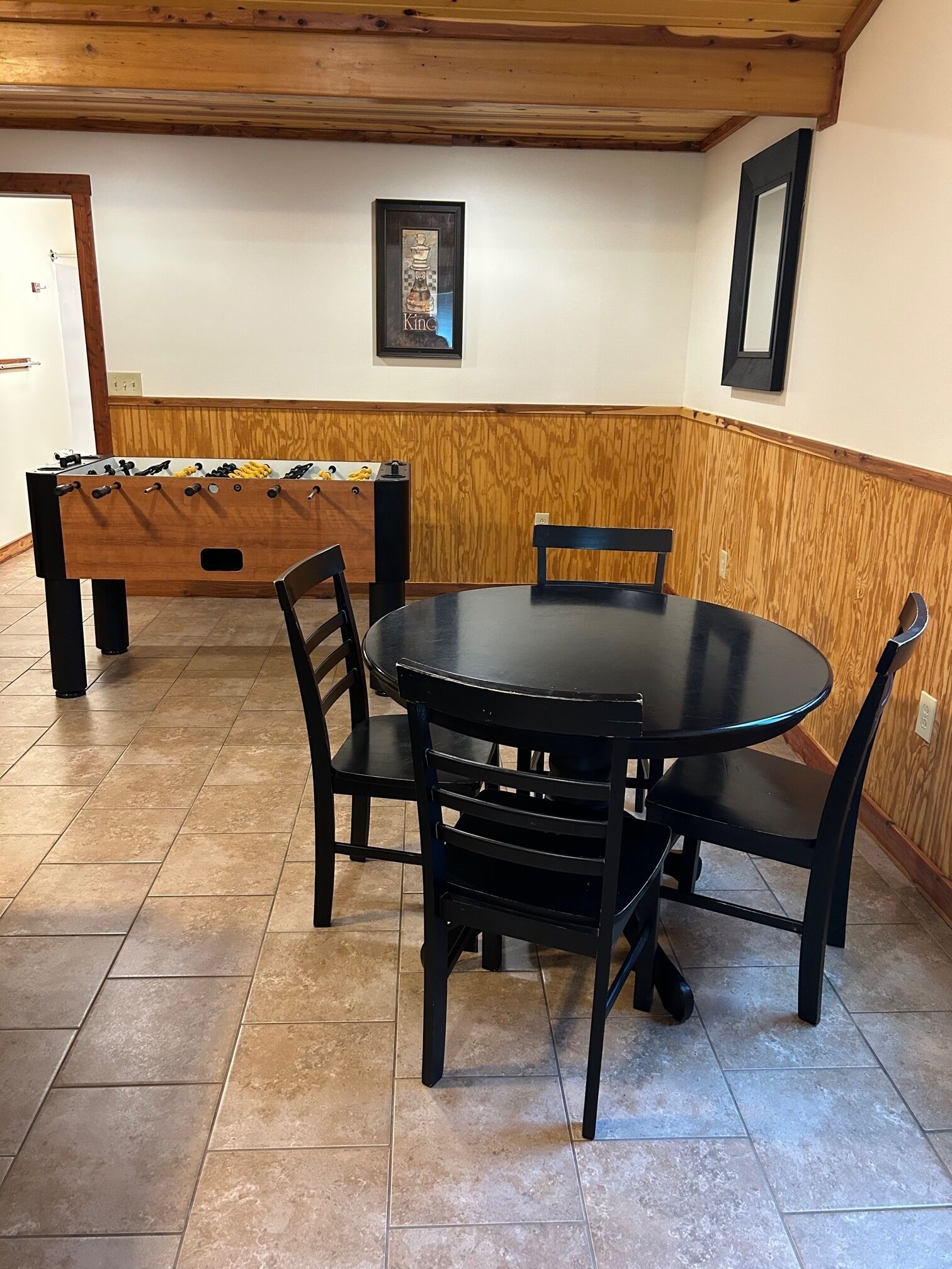 Un coin repas avec une table ronde et quatre chaises, un mur décoratif en bois et une table de baby-foot.