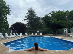Une piscine avec des chaises longues blanches et une personne se détendant dans l’eau.