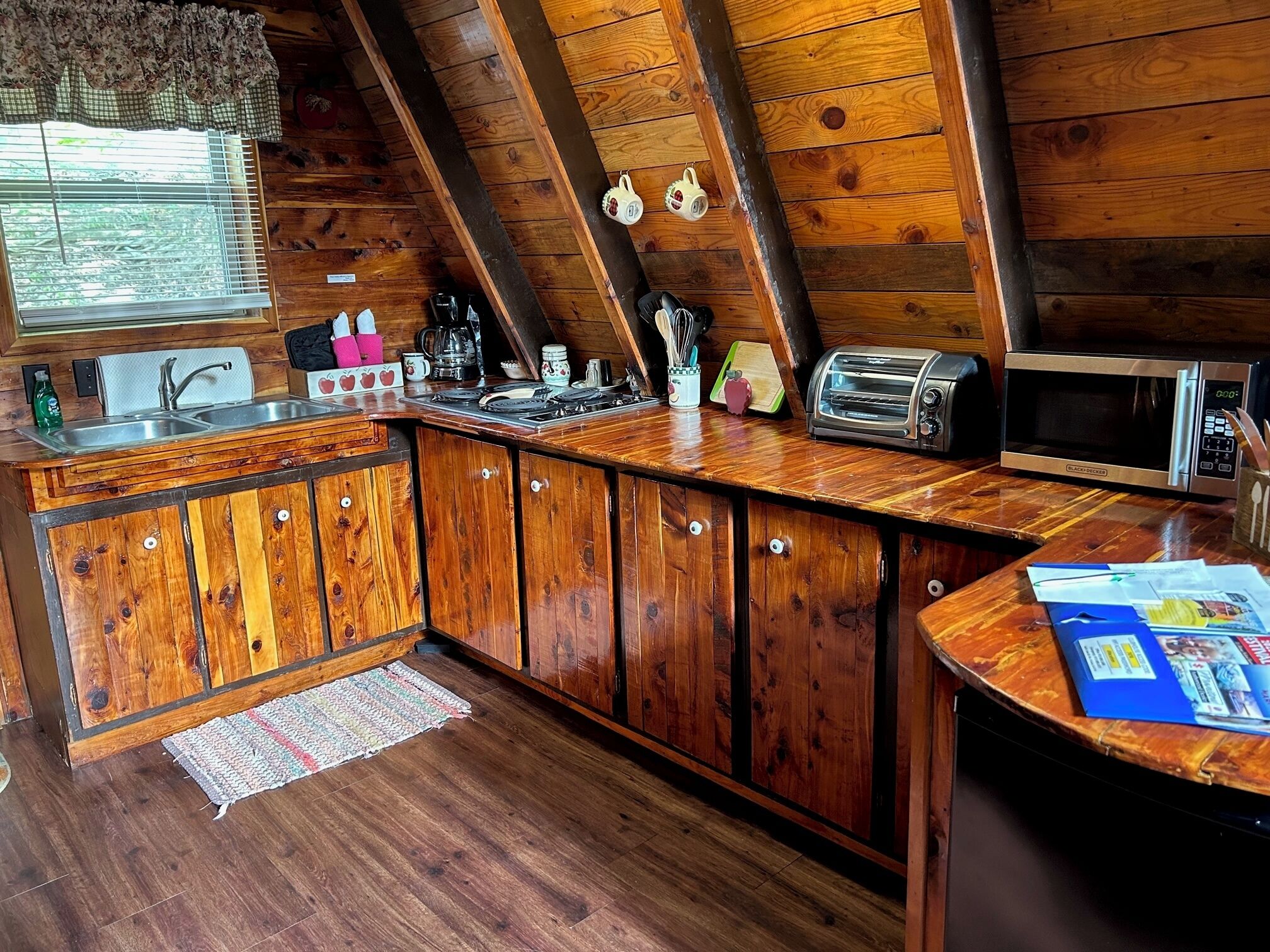 A rustic kitchen with wooden cabinets, a sink, a toaster, a kettle, and a microwave.