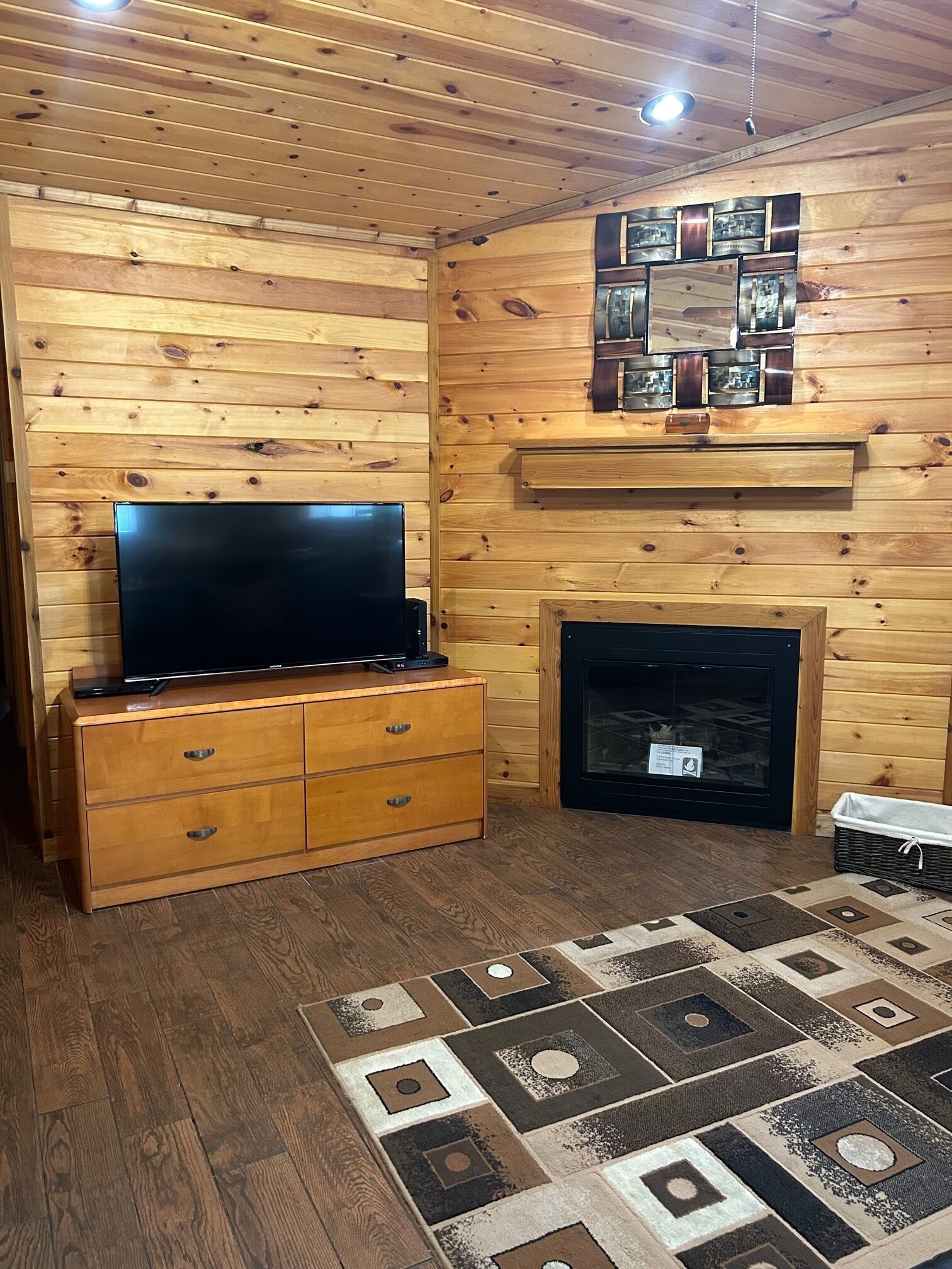 A wooden-paneled room with a flat-screen TV on a wooden cabinet, a fireplace, and a patterned rug.