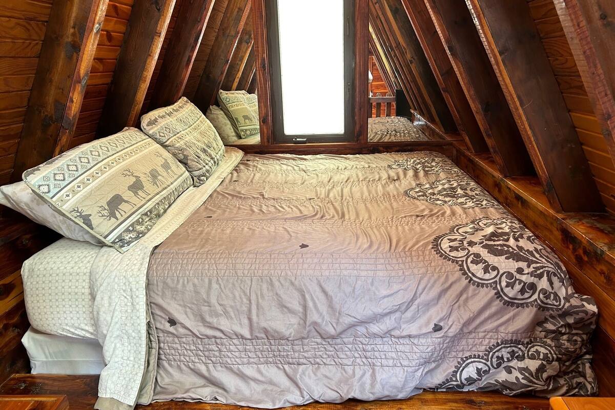 A cozy attic bedroom with a large bed, wooden beams, and a window.