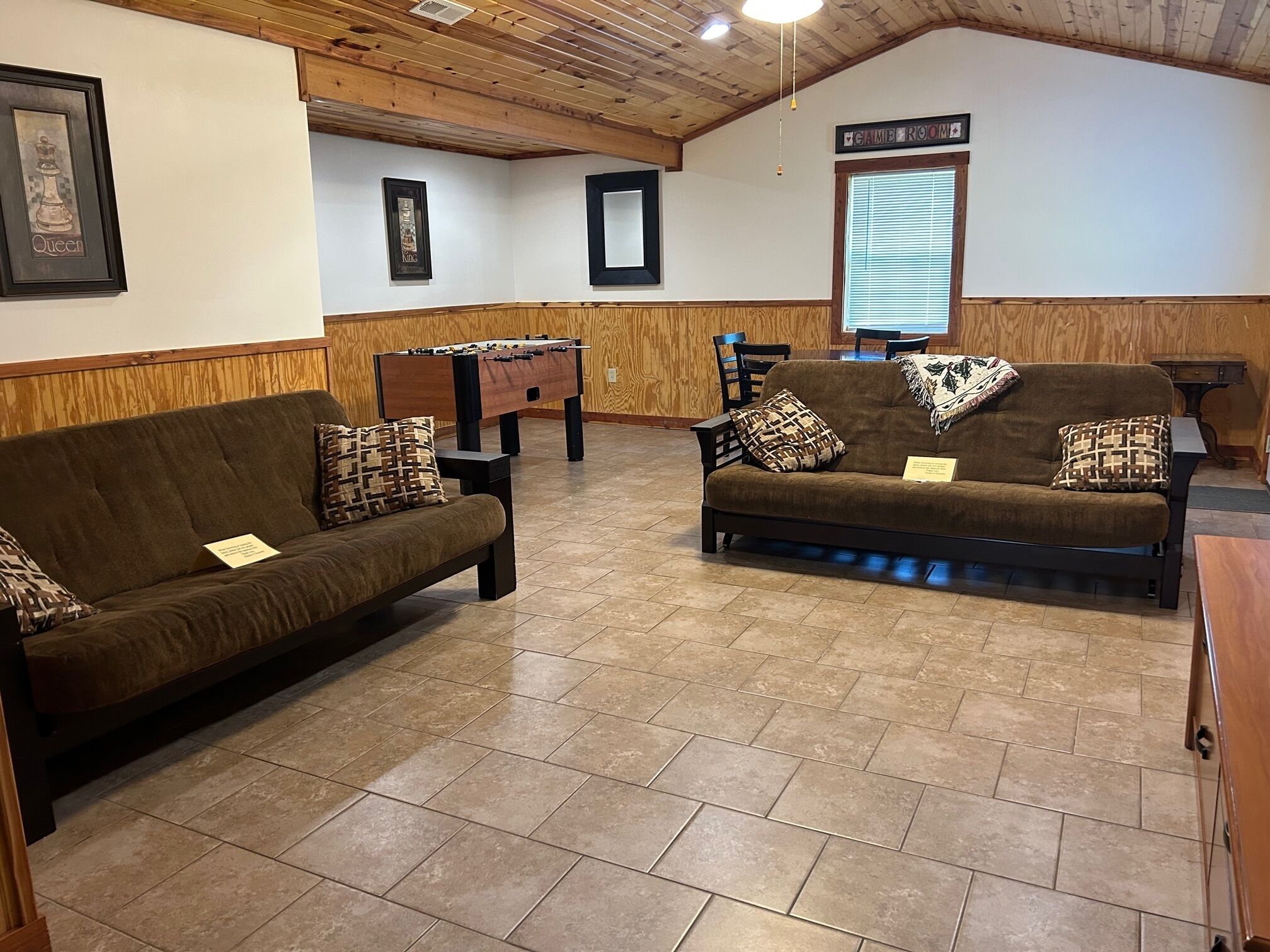 A cozy room with two sofas, a foosball table, wooden paneling, and a sign indicating a game room.