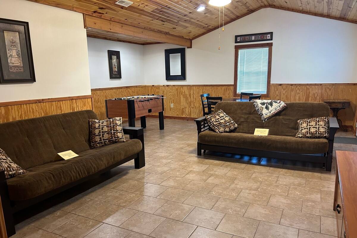 A cozy room with two sofas, a foosball table, wooden paneling, and a sign indicating a game room.