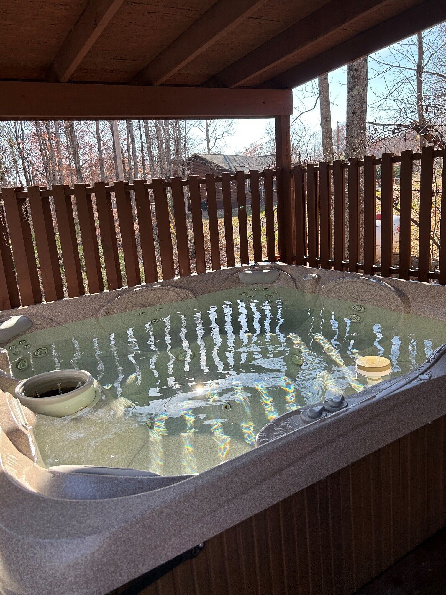 Een hottub onder een houten pergola, met een houten hek op de achtergrond.
