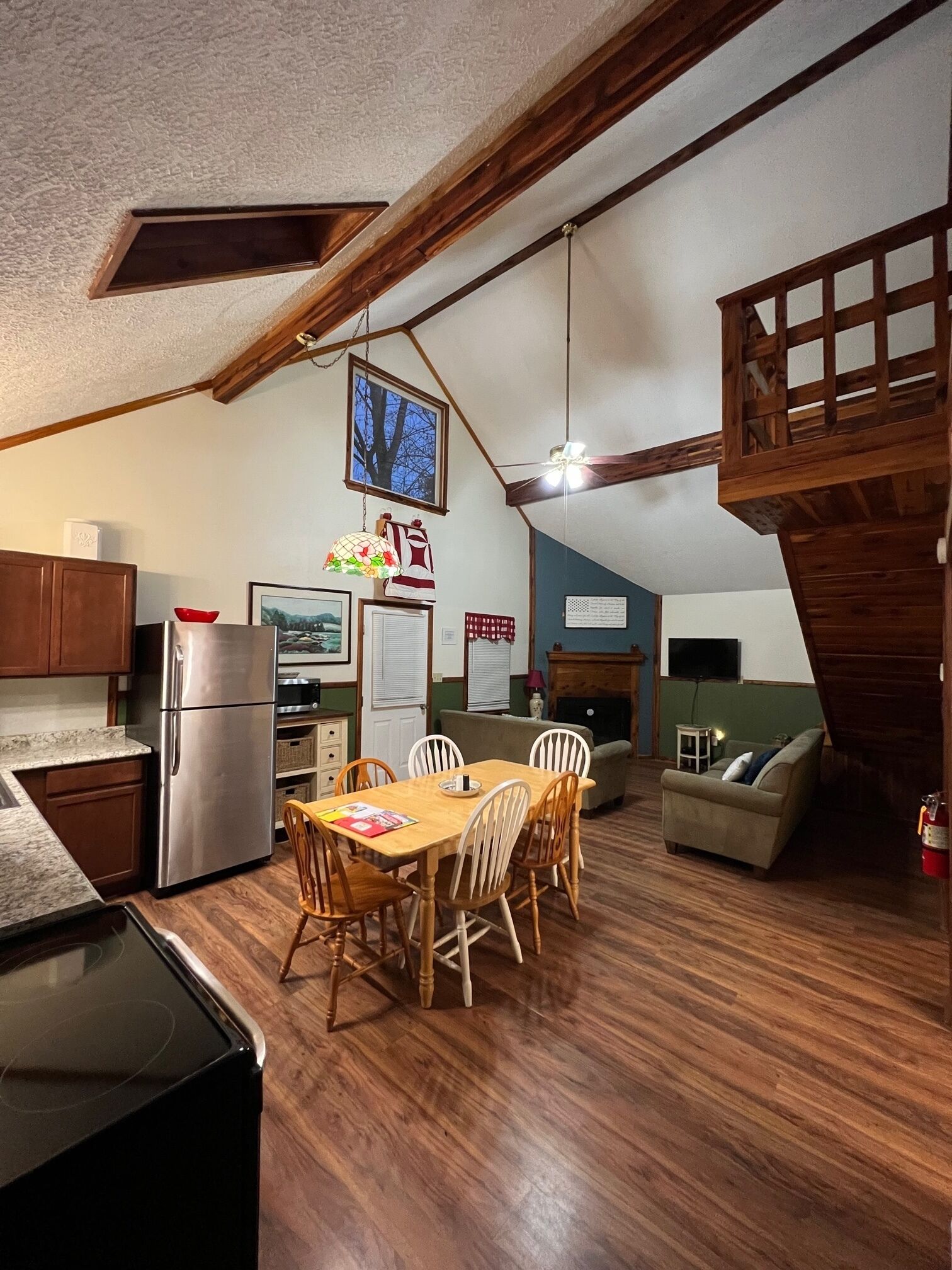A cozy kitchen with wooden beams, a dining area with a table and chairs, and a living space with a sofa and a television.