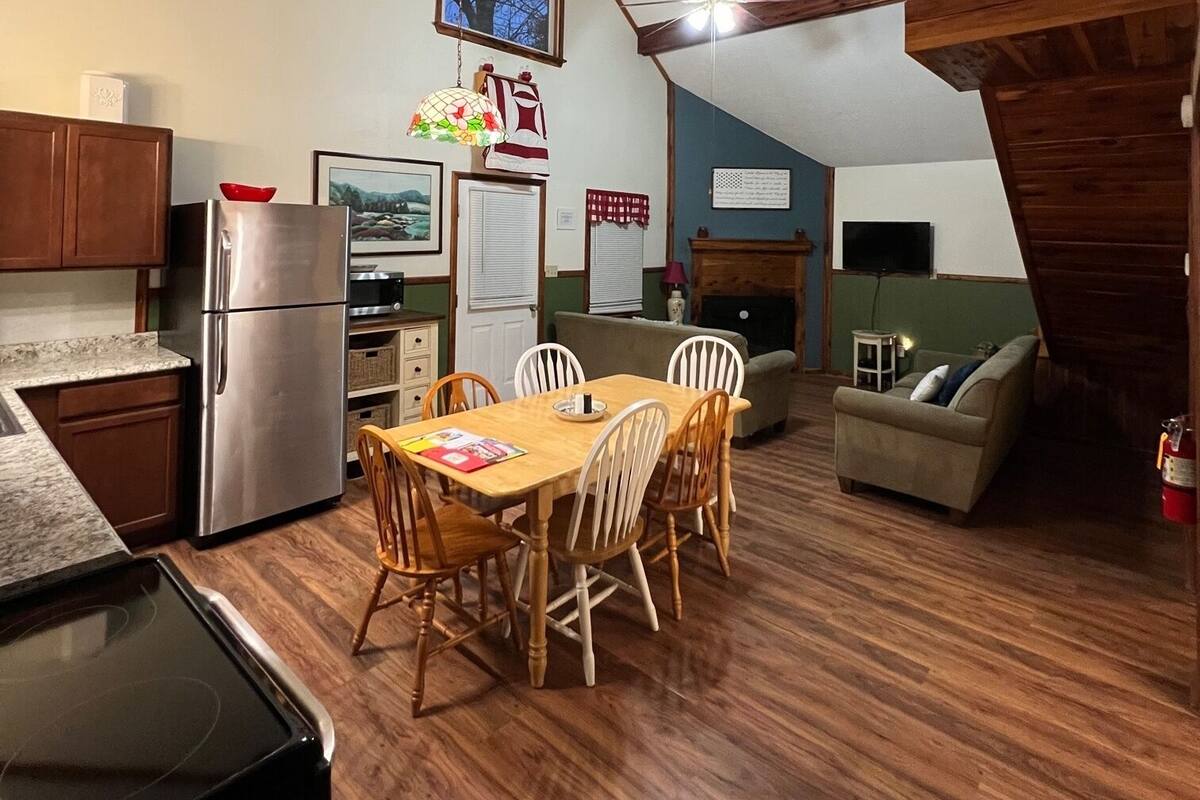 A cozy kitchen with wooden beams, a dining area with a table and chairs, and a living space with a sofa and a television.