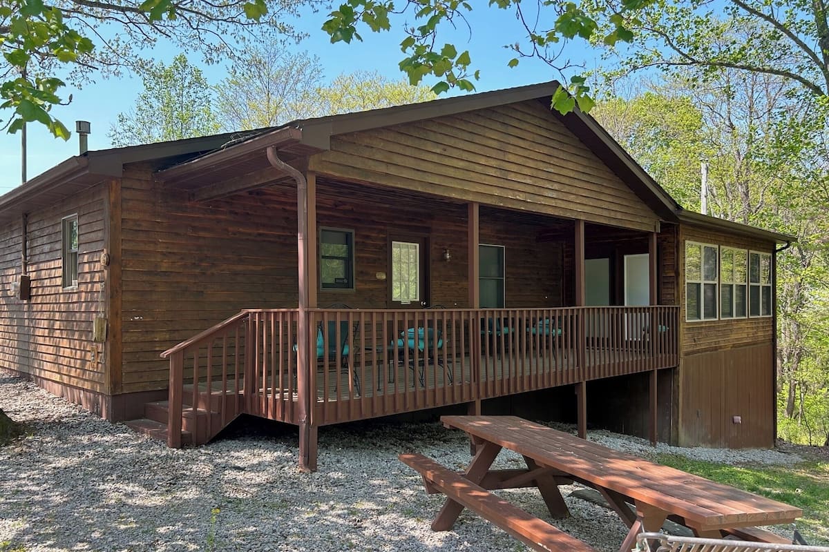 A wooden cabin with a covered porch, a picnic table, and a small deck area.