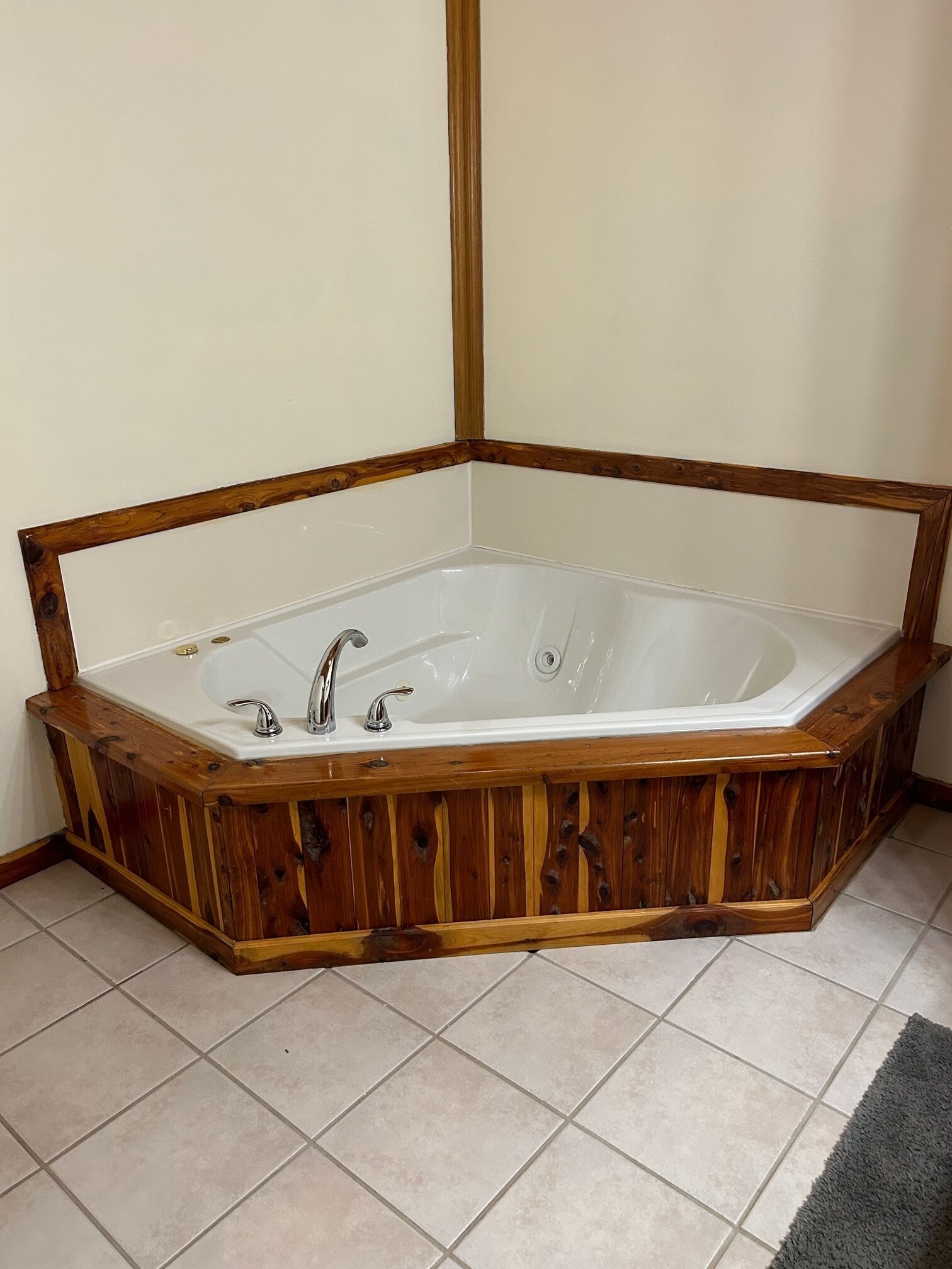 A corner bathtub with wooden framing and two faucets.