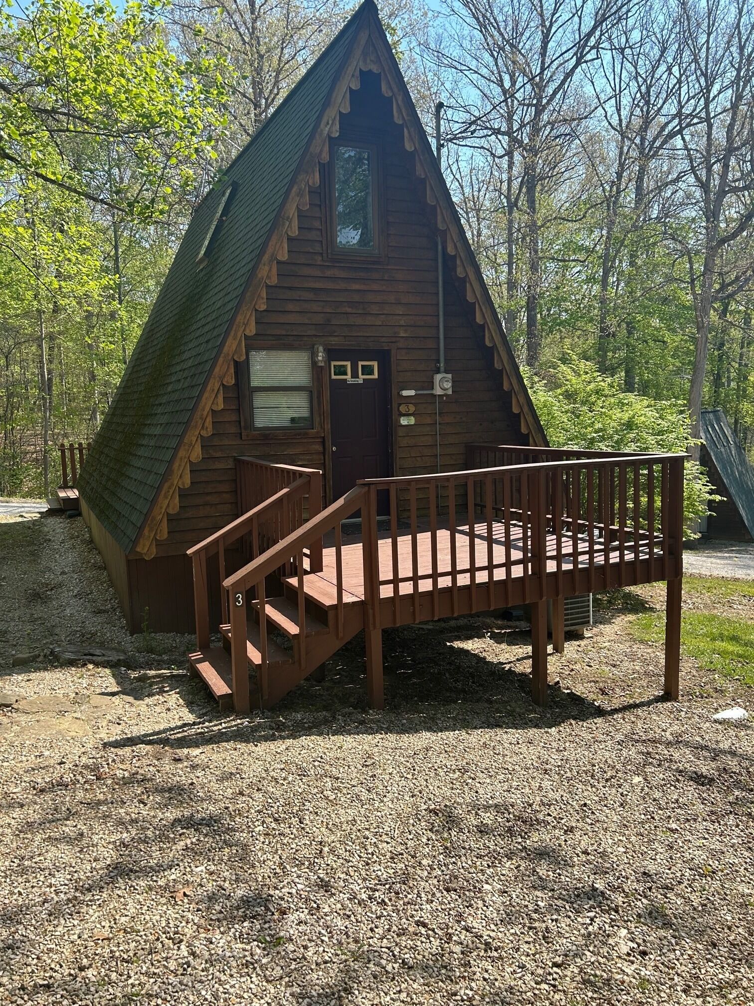 A wooden cabin with a steeply pitched roof, a front door, and a wooden staircase leading to a deck.