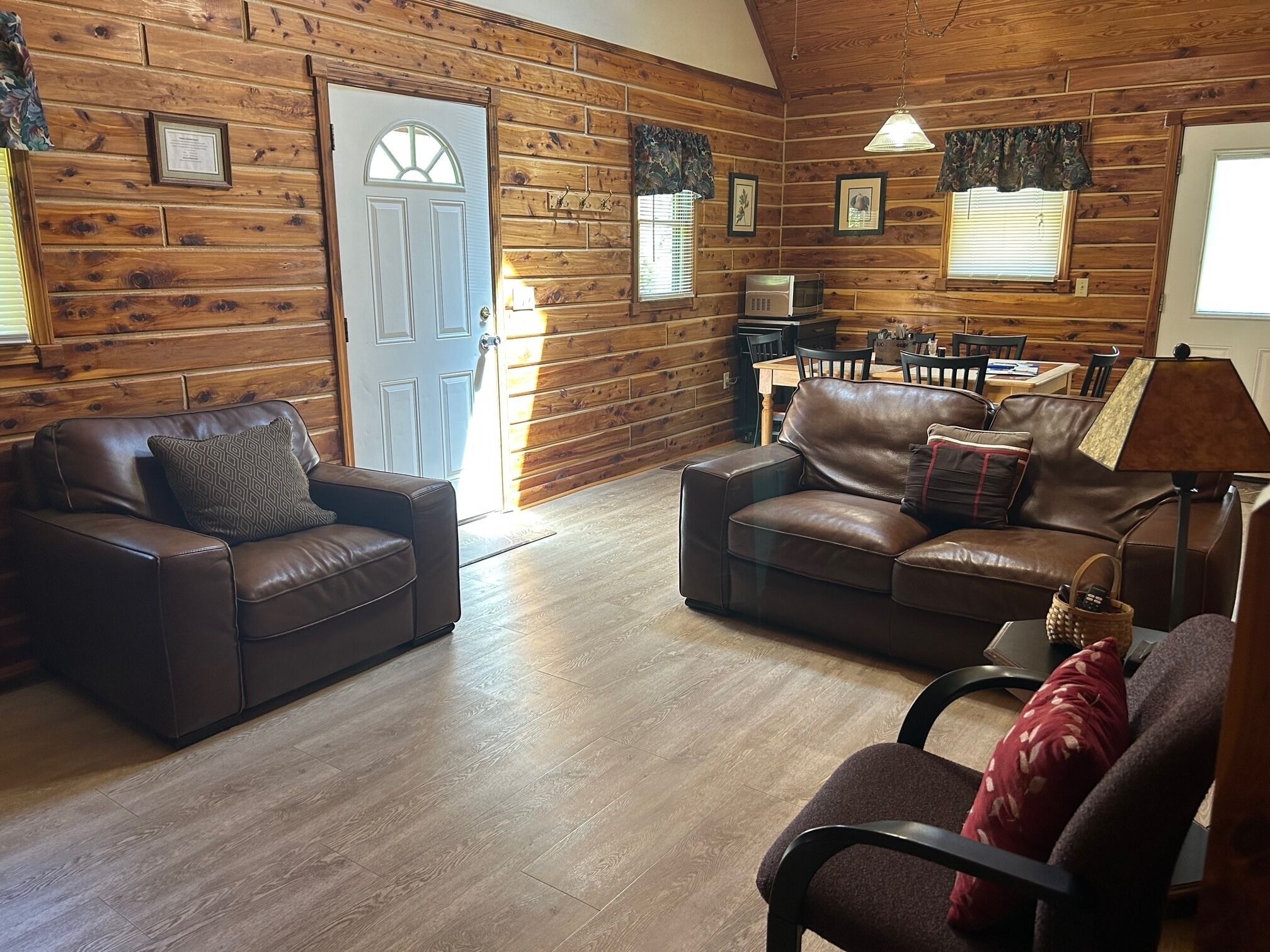 L’intérieur d’un chalet confortable, avec deux canapés en cuir, une table à manger et une lampe.