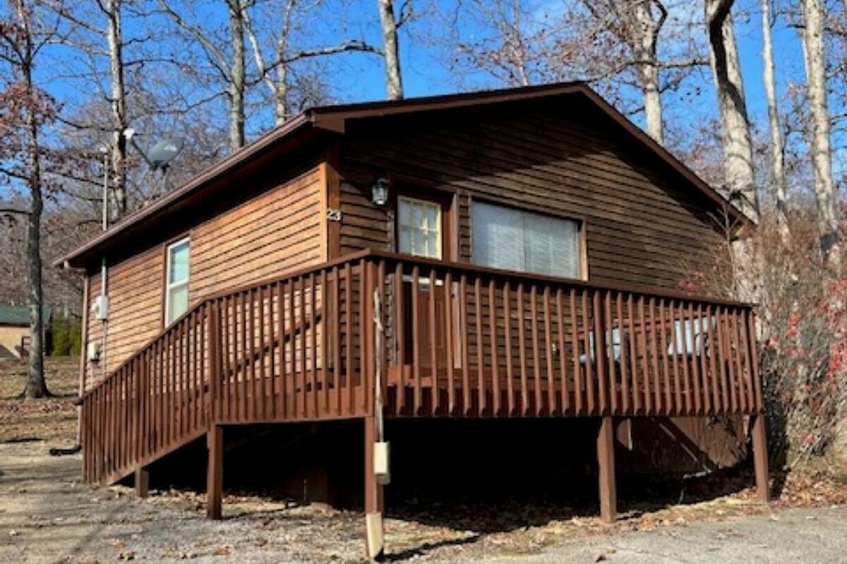 A wooden cabin with a deck, surrounded by trees.