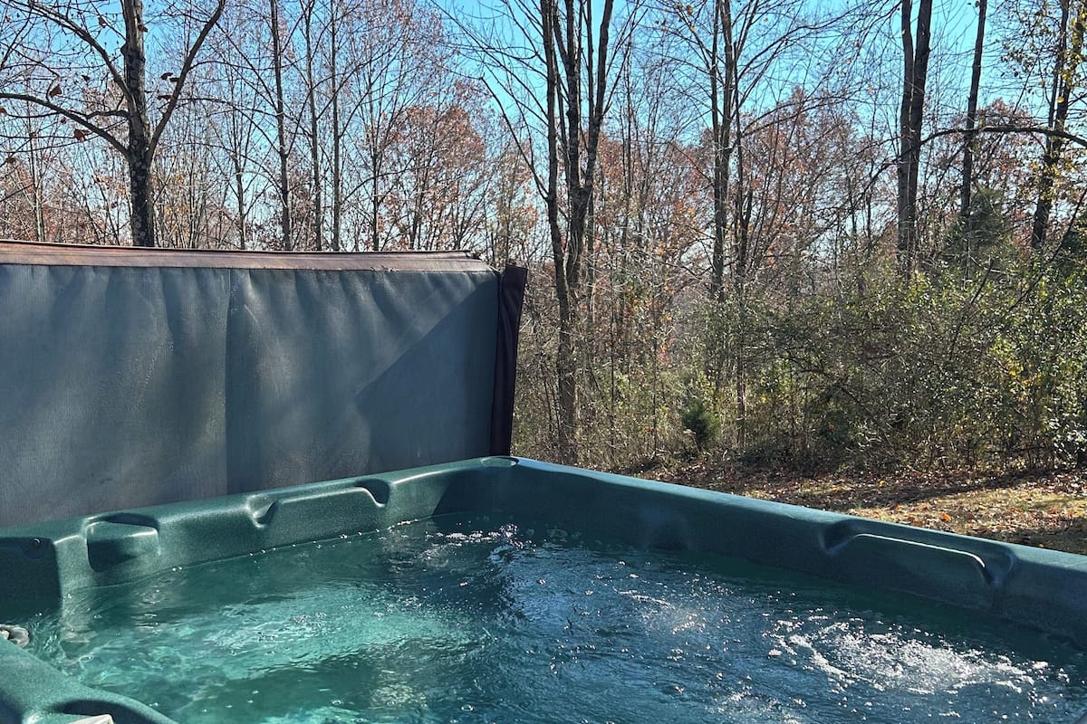 A hot tub with a wooden deck and a view of trees and sky.