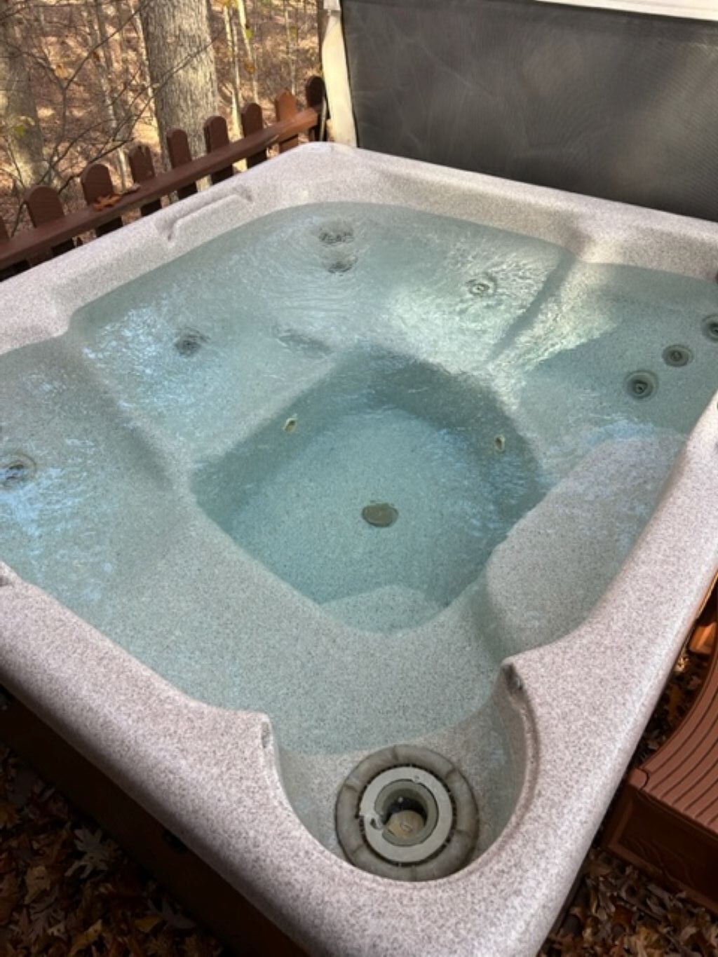 A hot tub with a rectangular shape, a drain in the center, and a wooden fence in the background.