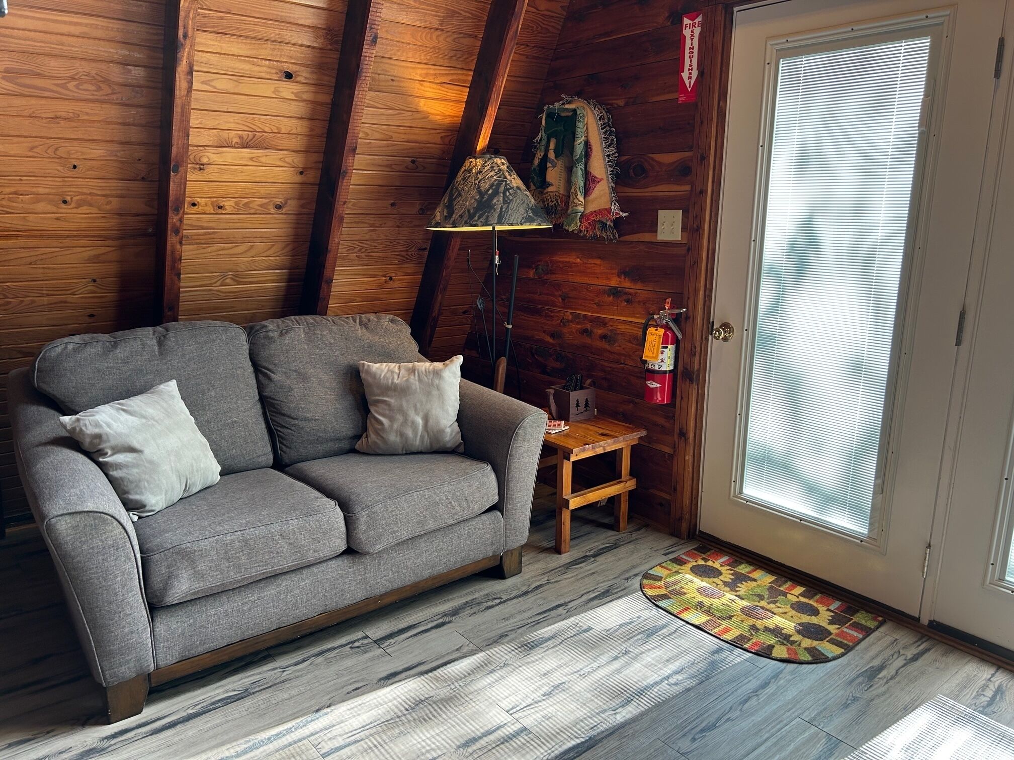 Une pièce chaleureuse avec un canapé gris, une petite table en bois, une lampe et un extincteur.