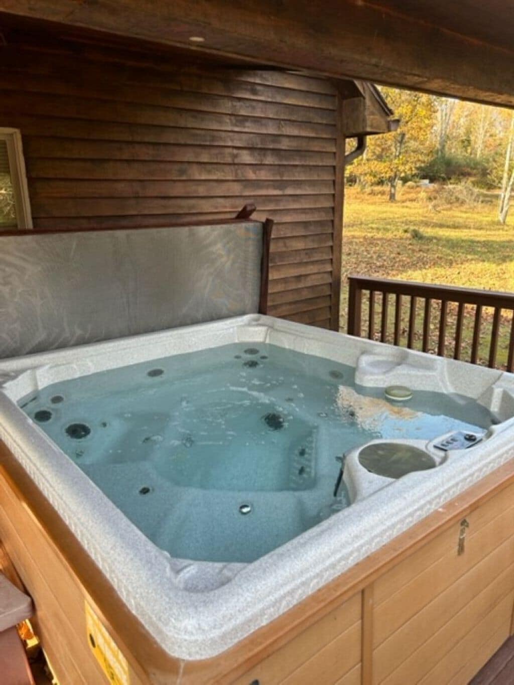 A hot tub in a wooden cabin with a view of a grassy field.