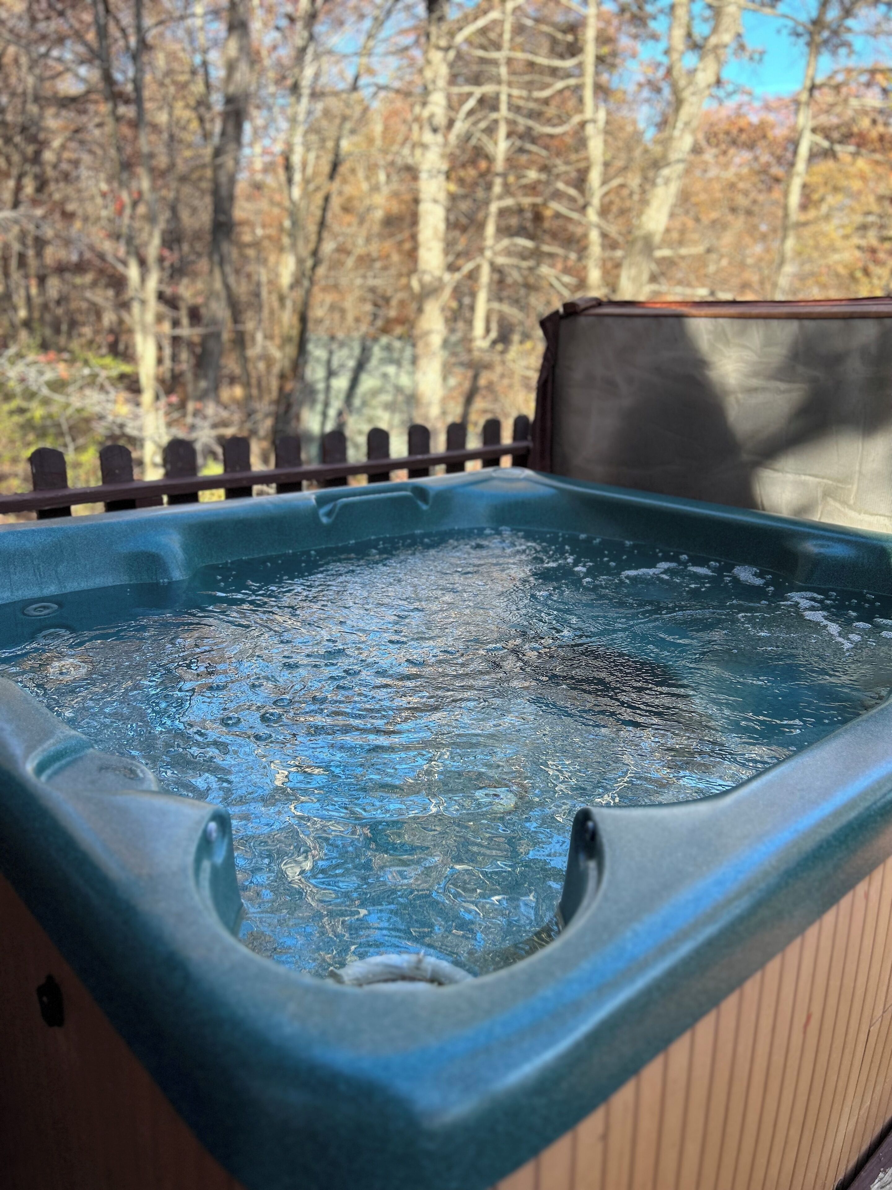 A hot tub with a wooden deck and a wooden fence in the background.