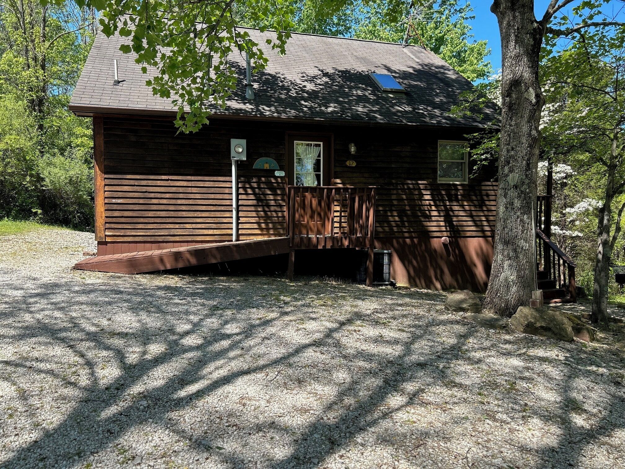 A wooden cabin with a porch, surrounded by trees.