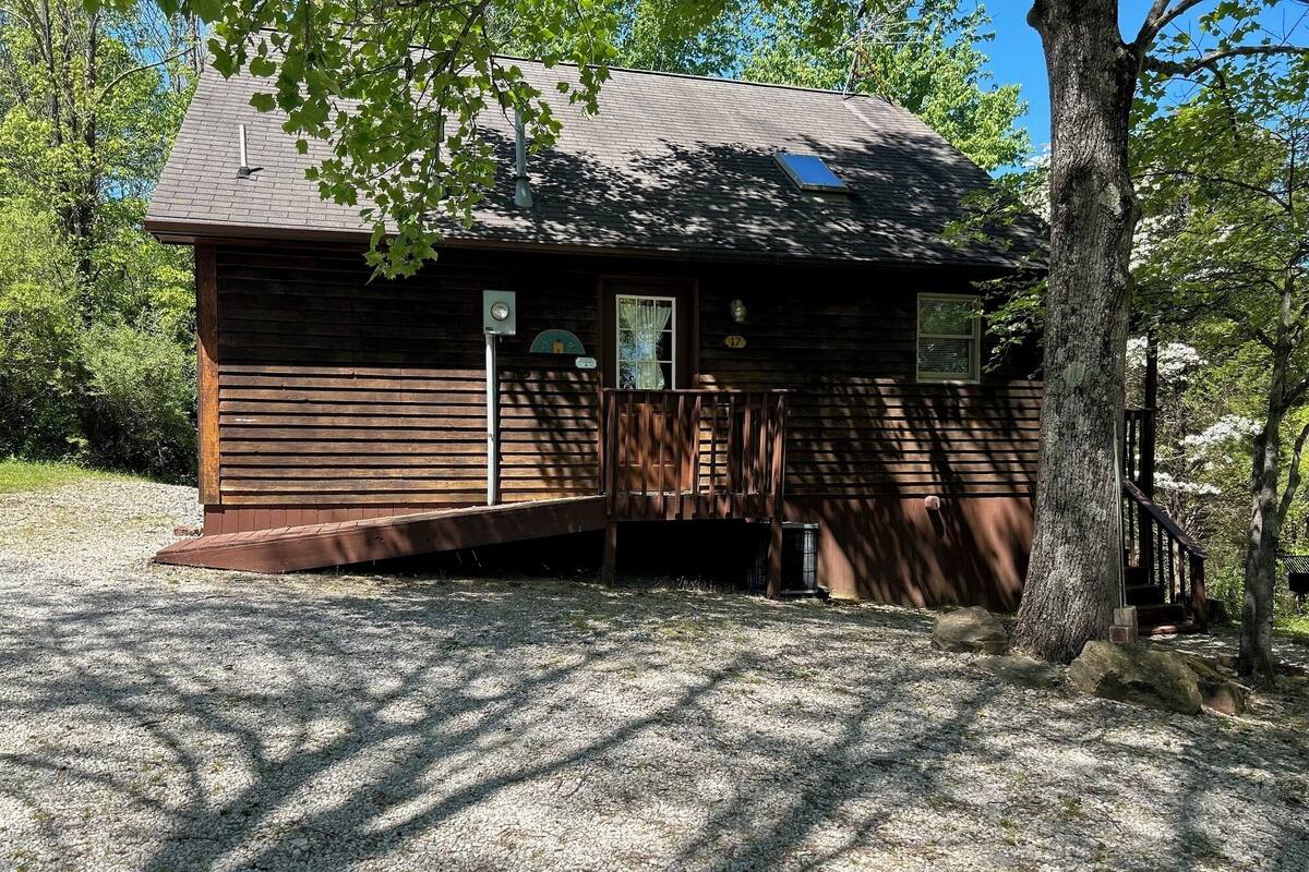 A wooden cabin with a porch, surrounded by trees.