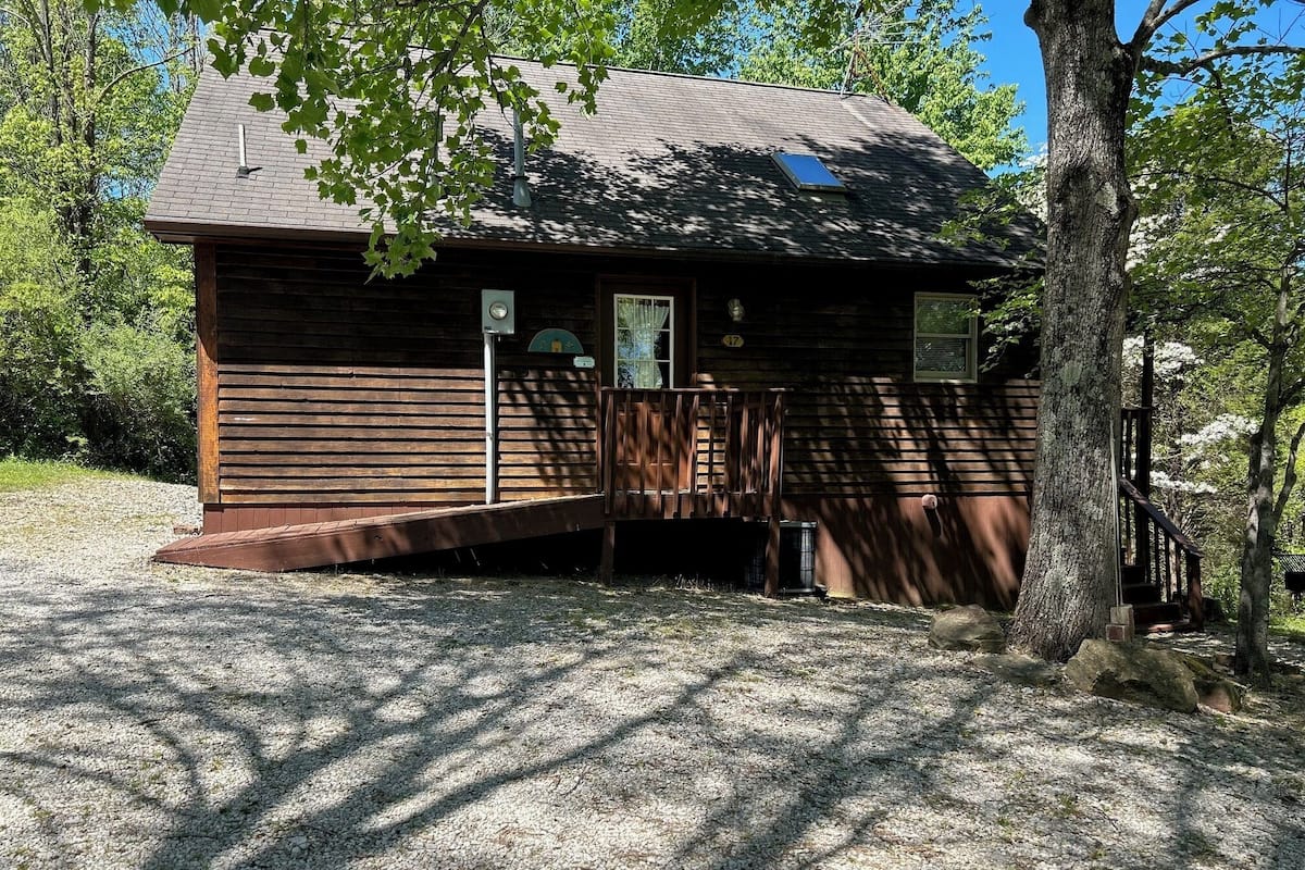 A wooden cabin with a porch, surrounded by trees.