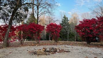 A gravel area with a stone fire pit surrounded by trees with red foliage.