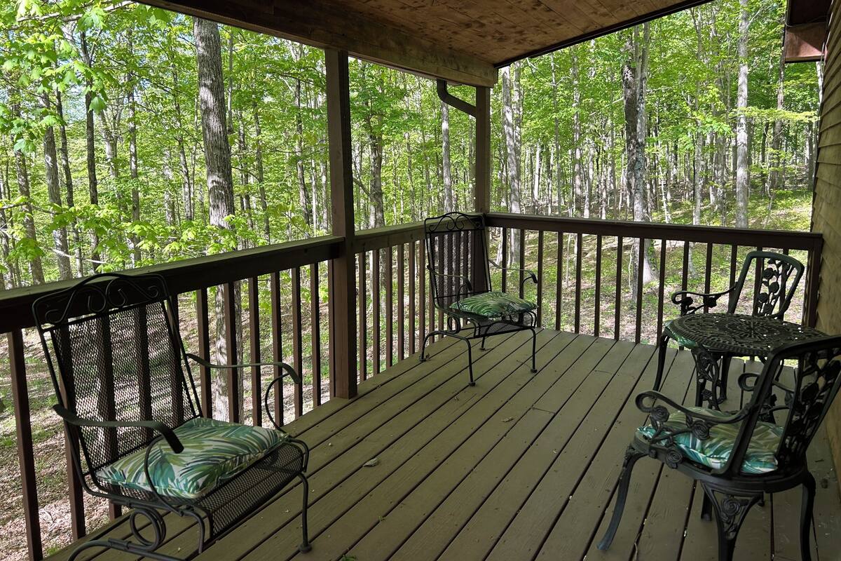 A covered porch with wooden railings, two metal chairs with cushions, and a table.