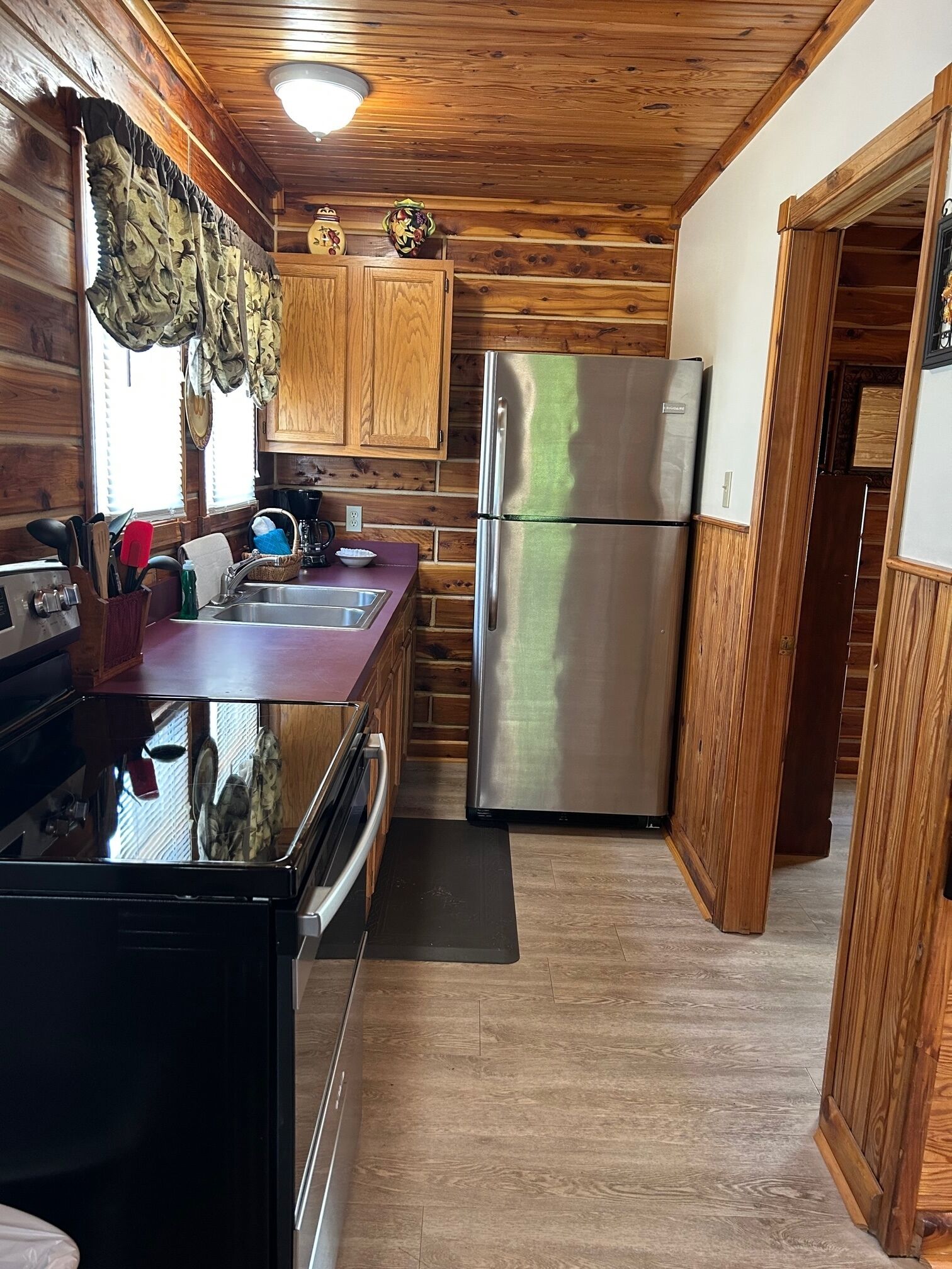 Una cocina compacta con paneles de madera, un refrigerador de acero inoxidable y un lavamanos con accesorios modernos.