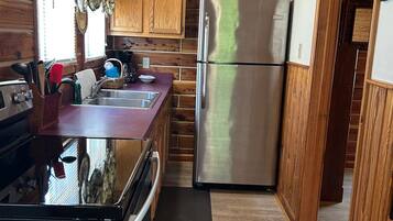 Una cocina compacta con paneles de madera, un refrigerador de acero inoxidable y un lavamanos con accesorios modernos.
