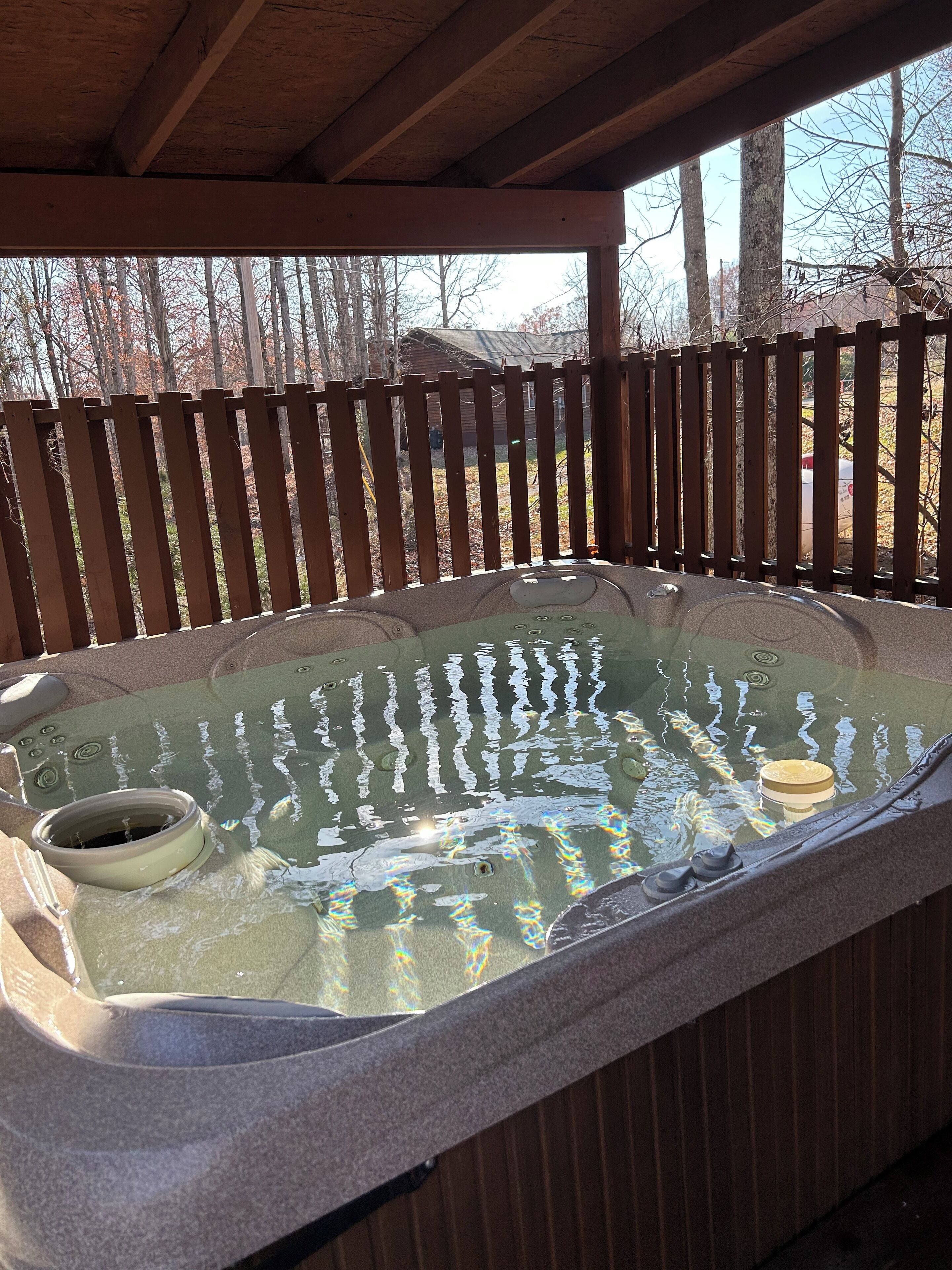 A hot tub under a wooden pergola with a wooden fence in the background.
