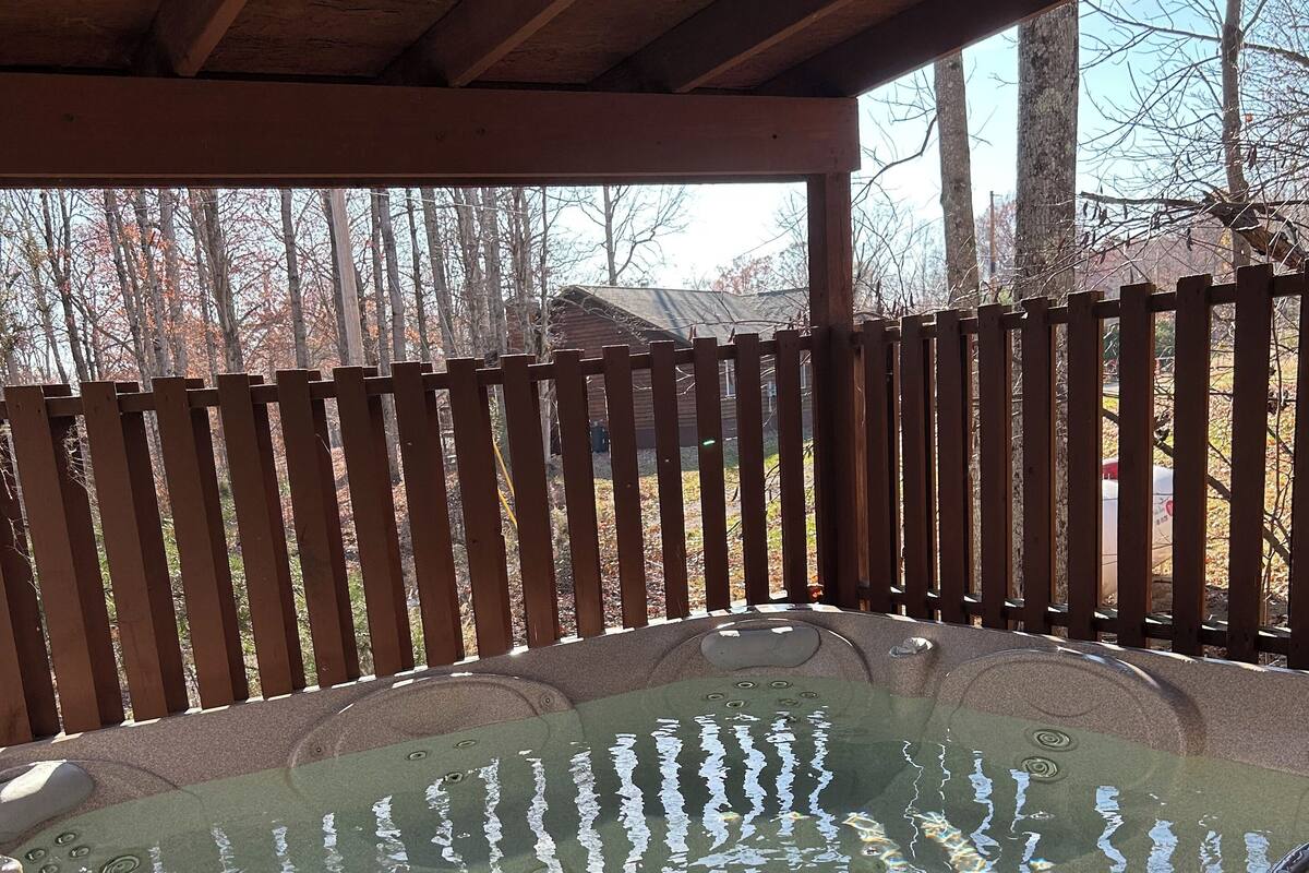 A hot tub under a wooden pergola with a wooden fence in the background.