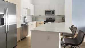Eine moderne Küche mit Edelstahl-Kühlschrank, Geschirrspüler, Mikrowelle und Backofen. Eine große Kochinsel mit Barhocker ist vorhanden.