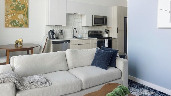 Een moderne woonkamer met een bank, een klein rond tafeltje en een keuken op de achtergrond.